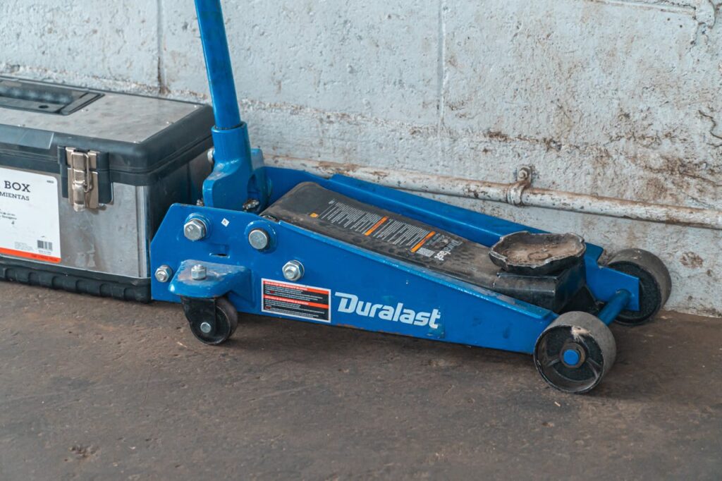 A blue hydraulic floor jack with a toolbox in an automotive garage setting.